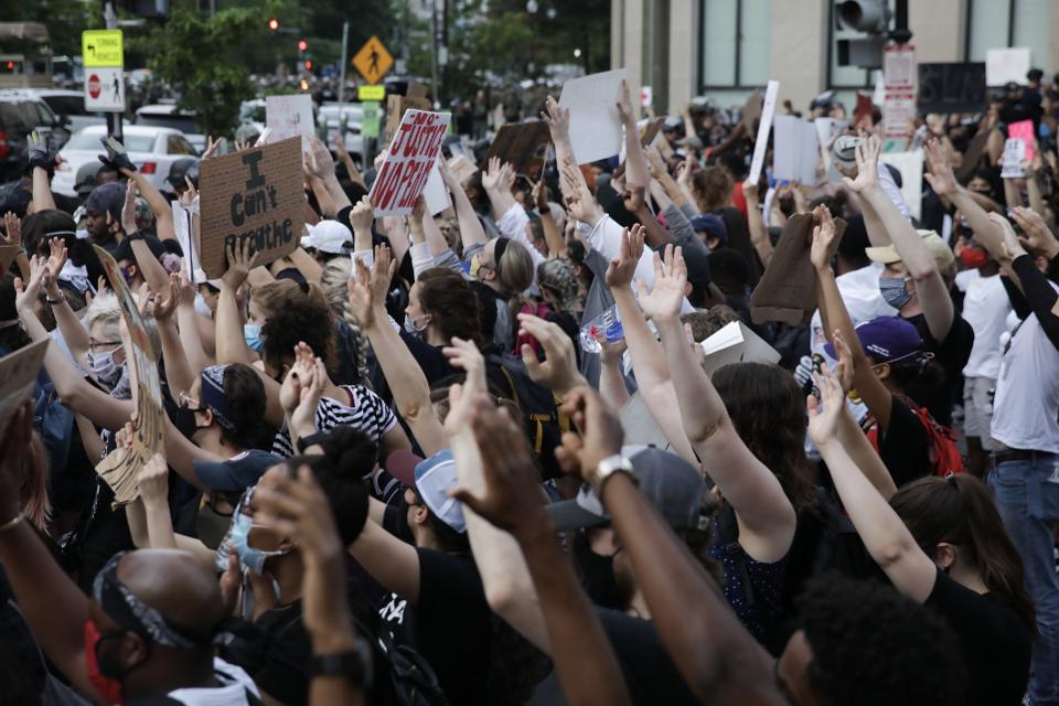 A densely packed crowd of people of all races raising their hands at a Washington, D.C., protest over the killing of George Floyd