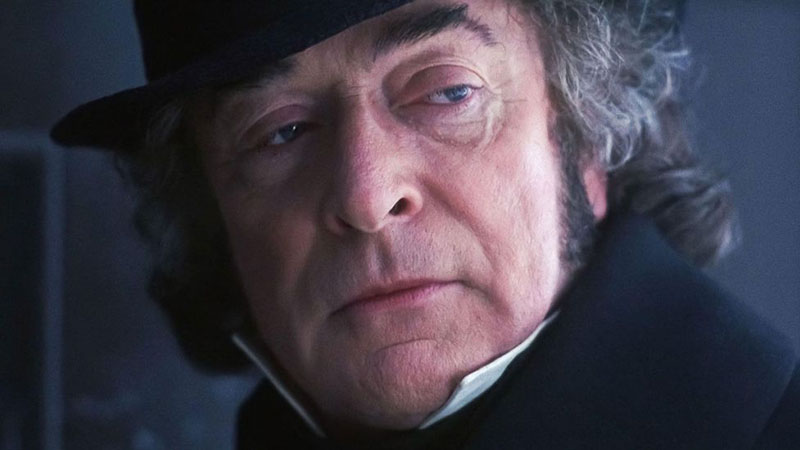 A screenshot from “The Muppet Christmas Carol,” showing Michael Caine as Ebenezer Scrooge, looking over his shoulder with disdain for the people of London and their Christmastime merriment, with the barest hint of bitterness as well and the merest possibility of sadness. All of which is right there on Michael Caine’s face.