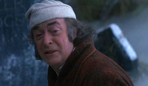 A screenshot from “The Muppet Christmas Carol,” showing Michael Caine as Ebenezer Scrooge in a snowy graveyard as he pleads with the Ghost of Christmas Yet to Come for mercy, and that a life can be changed and his miserable fate can be avoided. All of which is right there on Michael Caine’s face.