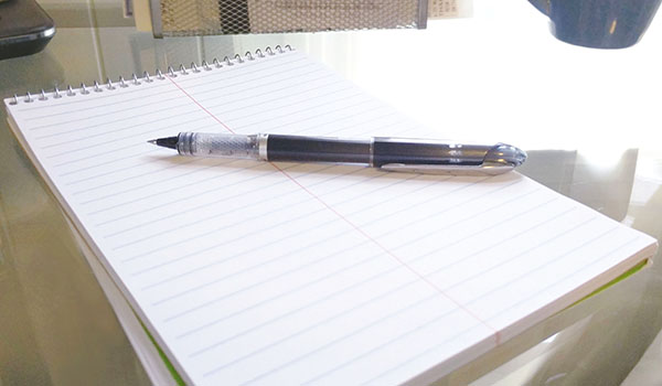 An uncapped pen lying on a lined notepad
