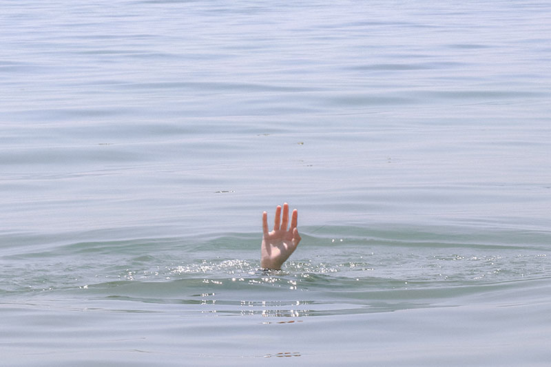 A long shot of a body of water — an ocean or lake or something — and toward the bottom, a hand sticking out of the water, just barely above the surface, as if in a last-ditch effort to get rescued before going under for good.