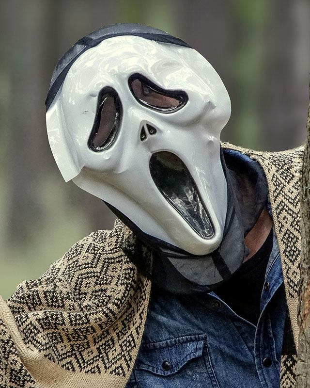 A chest-up shot of some person in a denim shirt with a patterned blanket over their shoulders and oh, yeah, the Ghostface mask from “Scream,” and the effect might be even creepier than if they were wearing the black robe.