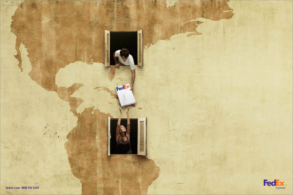 A 2010 award-winning FedEx ad by agency DDB Brazil. The image, which is advertising FedEx’s international delivery shows a huge wall, like the side of the building, with beige and tan plaster forming a rough world map showing North and South America. The wall has two open windows with open shutters — one in the U.S. area of the map, and one in the Brazil area. A man in a white t-shirt leans out of the “U.S.” window, handing a white FedEx package down to a woman in a black tank top who’s reaching out of the “Brazil” window to receive it. The FedEx logo is in the lower right-hand corner.