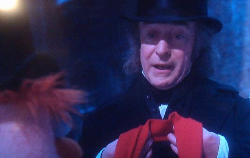 A screenshot from “The Muppet Christmas Carol,” showing Michael Caine as Ebenezer Scrooge accepting the gift of a red scarf from Beaker, whom he berated for trying to collect donations for the poor just the day before. Scrooge feels unworthy of such a gift, after the way he’s treated people throughout his life, but also deeply grateful, and touched, and a bit bewildered, and full of hope for the life he has before him. All of which is right there on Michael Caine’s face.