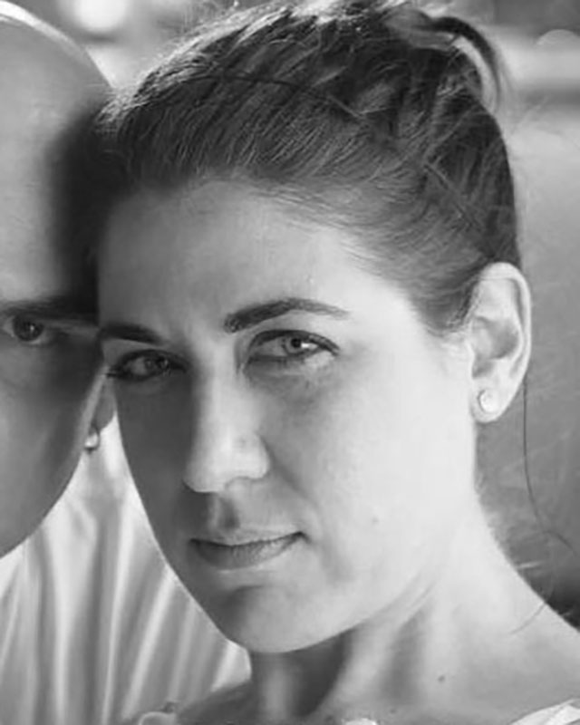 A black-and-white headshot of a white woman with her hair up in a bun, three-quarter facing the camera and glaring directly at us.