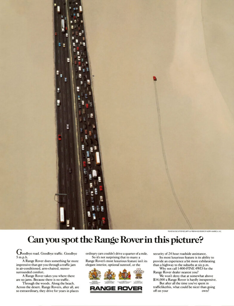 A large photo, shot from far above, showing a divided highway with a traffic jam on the side driving away from us and a smattering of cars on the side driving toward us. The road is cutting through what appears to be uninterrupted desert, but off to the right is tire tracks through the desert, parallel to the road, with the tiny red vehicle that left the tracks at the top. Below the photo are the words: “Can you spot the Range Rover in this picture? Goodbye road. Goodbye traffic. Goodbye 5 m.p.h. A Range Rover does something far more impressive than get you through a traffic jam in air-conditioned, arm-chaired, stereo-surrounded comfort. A Range Rover takes you where there are no jams. Because there is no traffic. Through the woods. Along the beach. Across the desert. Range Rovers, after all, are so extraordinary, they drive for years in places ordinary cars couldn’t drive a quarter of a mile. So it’s not surprising that to many a Range Rover’s most luxurious feature isn’t its elegant interior, optional sunroof, or the security of 24 hour roadside assistance. Its most luxurious feature is its ability to provide an experience a bit more exhilarating than a highway to the suburbs at six p.m. Why not call 1-800-FINE 4WD for the Range Rover dealer nearest you? We won’t deny that at somewhat above $34,000 a Range Rover is hardly inexpensive. But after all the time you’ve spent in trafficlikethis, what could be nicer than going off on your own?” Below the copy are four heraldry-style crests and the Range Rover logo.
