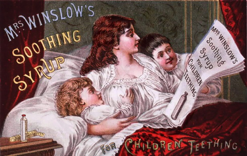 A very, very old, colorful ad showing a red-haired mother in a white nightgown lying in a bed with a red bedspread and white sheets and pillows, with matching red bed curtains to either side. She has a dark-haired boy and a blonde girl on either side of her, smiling as she reads a newspaper. On the bedside table to our left are a small glass bottle of morphine. At the top left, in decorative text, are the words, “Mrs. Winslow’s Soothing Syrup.” On the newspaper are the words, “Mrs. Winslow’s Soothing Syrup for Children Teething,” with an image of the same bottle sitting on the bedside table. At the lower right of the ad are the words, “For Children Teething.”