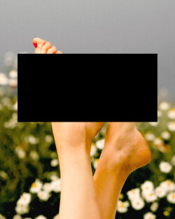 Photo of a woman’s feet from the ankle down, except up, because they’re pointed in the air against a background of white flowers and a blue sky. The feet are those of a white woman with red nail polish.